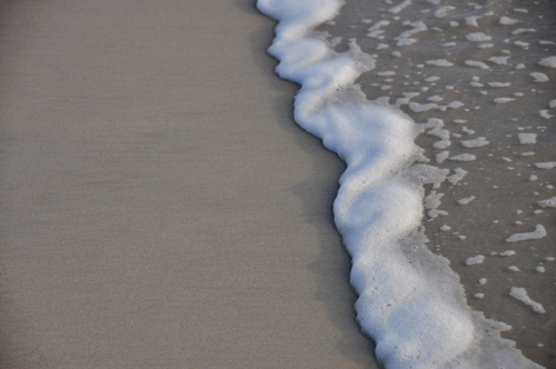 Free Picture: Photo of ocean foam washing up over the sand with a wave.