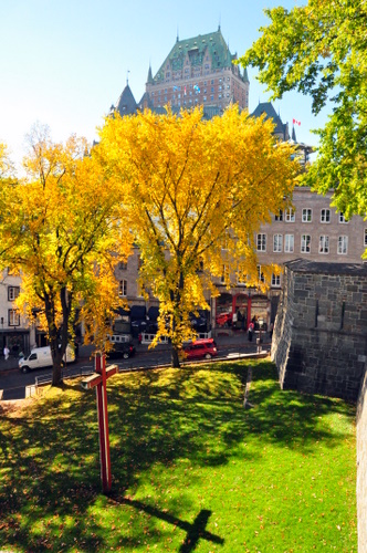 Free Picture: Photo of a unique picture of a cross casting its shadow on the green grass with Chateau Frontenac in the background in Quebec City, Canada.